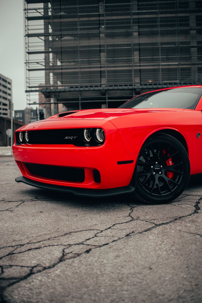 Close-up of a red Dodge Challenger parked on urban concrete pavement, showcasing luxury and sports car appeal.